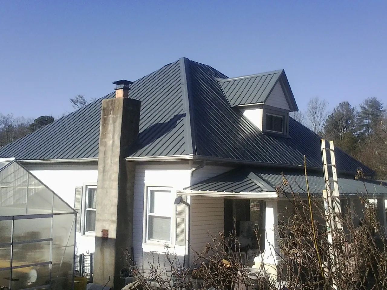 Dark blue standing seam metal roof on a white farmhouse with dormer — Slate & Tile Roof Repair by Roofing Brothers in Honeyville