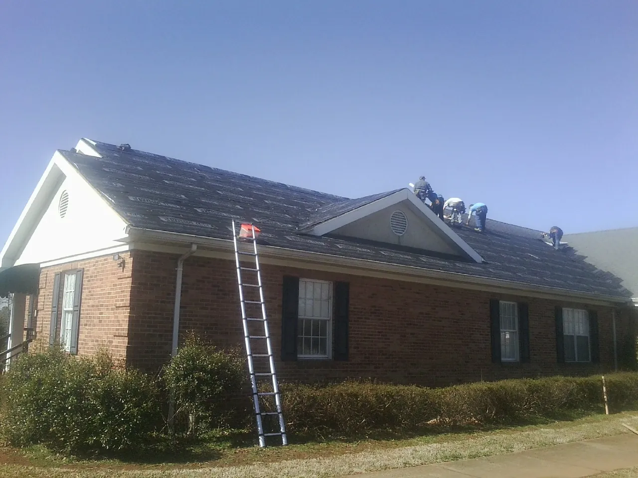 Crew tearing shingles off a brick ranch roof with a ladder set — Metal Roof Repair work by our crew in Honeyville