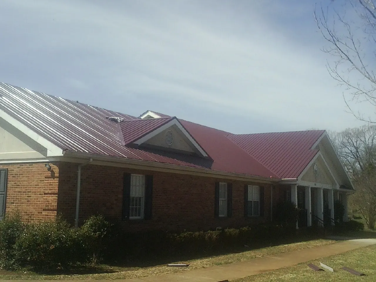 Red metal roof with gabled entries on a long brick building, from a Hail Damage Roof Repair job in Honeyville