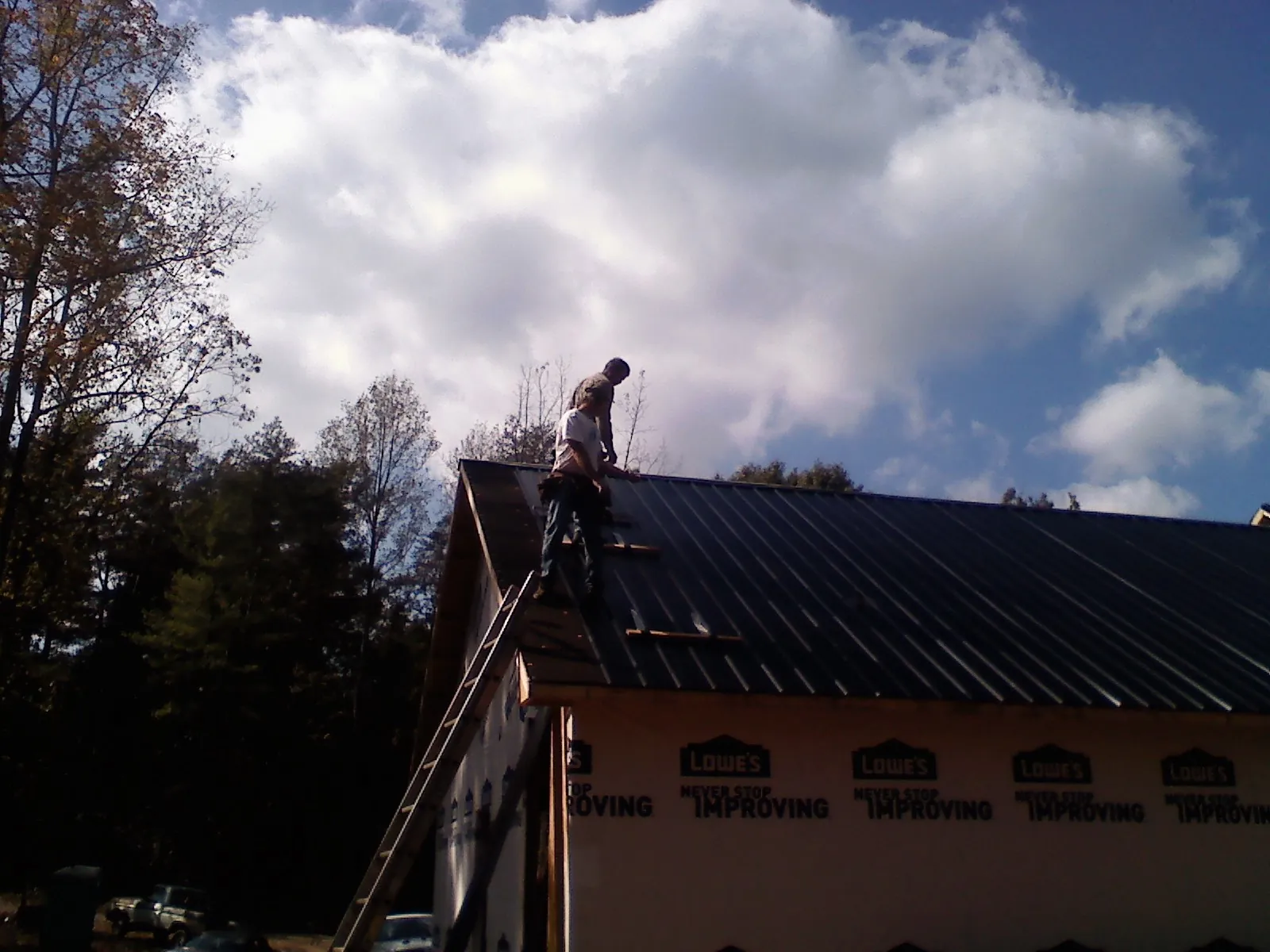 Roofer fastening dark metal panels high against a cloudy sky, from a Roof Inspection job in Honeyville