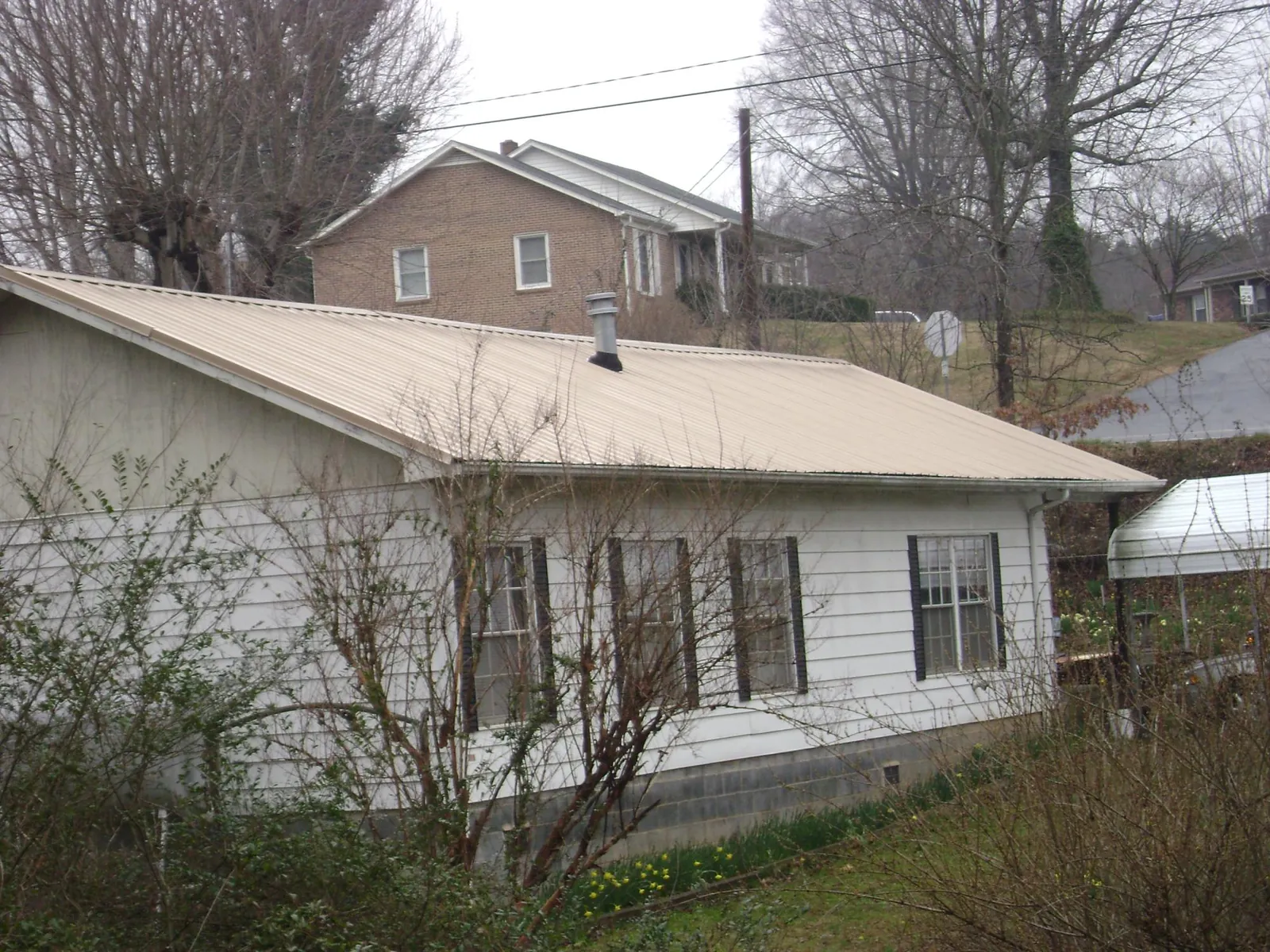 Tan metal roof on a white sided house set into a hillside — Commercial Roofing by Roofing Brothers in Honeyville